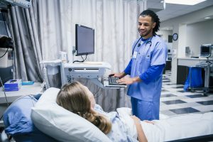 New RN Grad Jobs - a nurse speaking with a patient bedside.