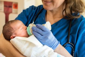 Nurse Midwife Certification: Everything You Need to Know - a picture of a nurse midwife bottle feeding a newborn baby. 