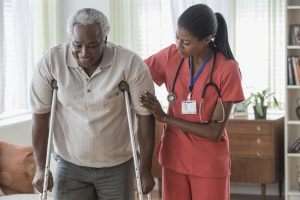 In-Home Care Nurse Career Guide 2022 - a picture of a nurse helping a patient on crutches.