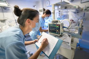 NICU Nurse: How to Become a Neonatal Nurse - a picture of a NICU nurses working together with a newborn in an incubator.