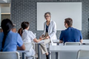 Nurse Teacher (aka Nurse Educator)_ The Complete Career Guide - a picture of a nurse educator sitting at the front of the classroom speaking with a student.